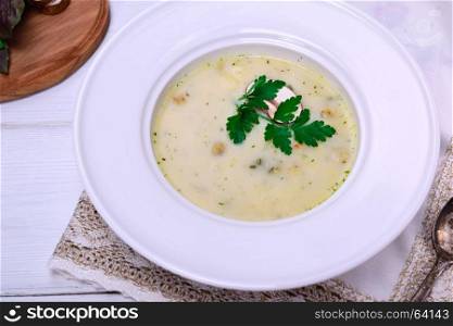 mushroom soup in a white round plate on a white wooden background, top view