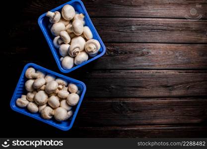 Mushrooms in a plastic box on the table. On a wooden background. High quality photo. Mushrooms in a plastic box on the table.