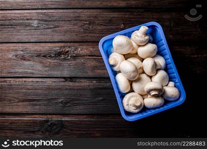 Mushrooms in a plastic box on the table. On a wooden background. High quality photo. Mushrooms in a plastic box on the table.