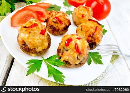 Mushrooms stuffed with meat and peppers with parsley and tomatoes in the white plate on a napkin, fork on the background of wooden boards