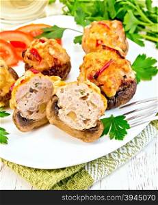 Mushrooms stuffed with meat whole and sliced parsley and tomatoes in a white plate on a towel, fork on a wooden boards background