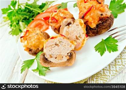 Mushrooms stuffed with meat whole and sliced parsley and tomatoes in a white towel on a plate, fork on the background light wooden boards