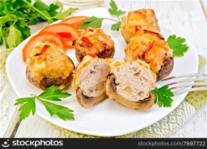 Mushrooms stuffed with meat whole and sliced parsley and tomatoes in a white plate on a napkin, fork on the background of wooden boards