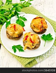 Mushrooms stuffed with meat with parsley and tomatoes in a white plate on a green kitchen towel, fork on the background of wooden boards