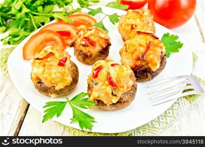 Mushrooms stuffed with meat with parsley and tomatoes in a white plate on a green towel, fork on a wooden boards background