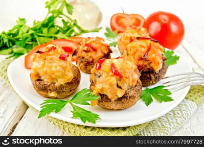 Mushrooms stuffed with meat with parsley and tomatoes in a white plate on a towel, fork on a wooden boards background