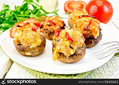 Mushrooms stuffed with meat with parsley and tomatoes in a white towel on a plate, fork on the background light wooden boards