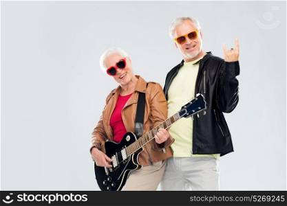 music, age and people concept - happy senior couple in sunglasses with electric guitar showing rock hand sign. senior couple with guitar showing rock hand sign
