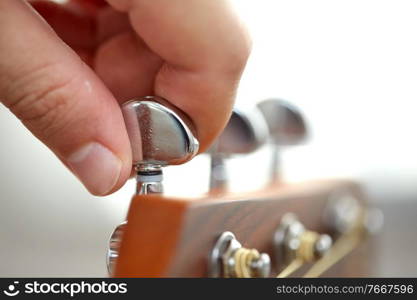 music and musical instruments concept - close up of hand tuning guitar strings with pegs. close up of hand tuning guitar strings with pegs