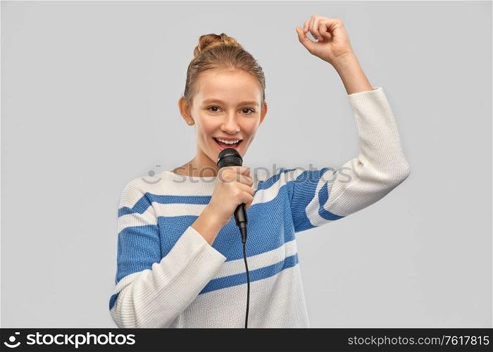 music and people concept - smiling teenage girl in pullover with microphone singing over grey background. smiling teenage girl with microphone singing