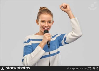 music and people concept - smiling teenage girl in pullover with microphone singing over grey background. smiling teenage girl with microphone singing