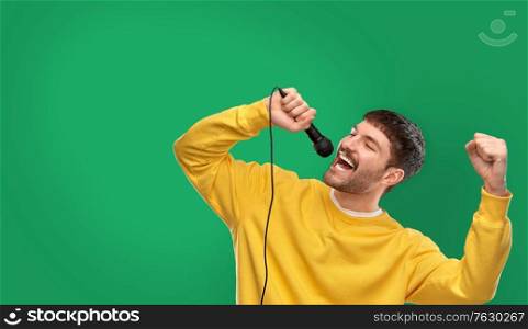 music and people concept - young man in yellow sweatshirt with microphone singing over emerald green background. man in yellow sweatshirt with microphone singing