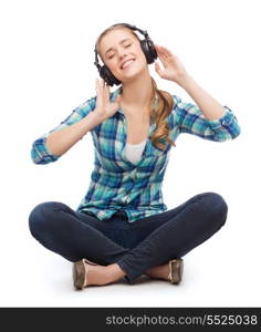 music and technology concept - smiling young woman sitting on floor and listeting to music with headphones