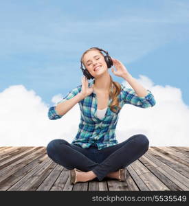 music and technology concept - smiling young woman sitting on floor and listeting to music with headphones