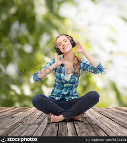 music and technology concept - smiling young woman sitting on floor and listeting to music with headphones