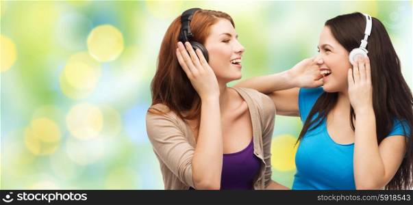 music and technology concept - two laughing teenage girls or young women with headphones listening to music over green lights background. two happy girls with headphones listening to music