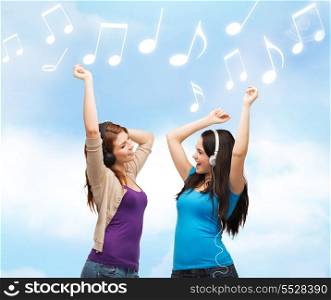 music and technology concept - two laughing teenagers with headphones dancing over blue sky background and music notes
