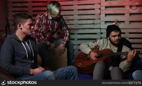 Music band creating a new hit together, guitarist picking chords, drummer setting the beat and the rest of members writing lyrics. Teenage rock band jamming and practicing in garage. Lifestyle of youngsters.
