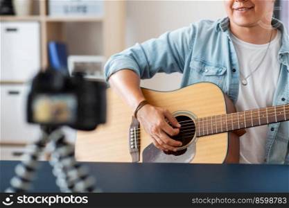 music, blogging and people concept - close up of male guitarist or musician with camera playing acoustic guitar and recording video or live streaming at home. man with camera playing guitar and recording video