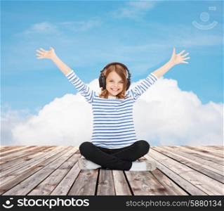 music, childhood, people and technology concept - happy girl with headphones listening to music over blue sky and cloud background