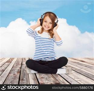 music, childhood, people and technology concept - happy girl with headphones listening to music over blue sky and cloud background