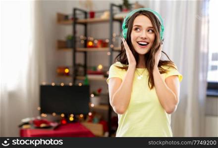 music, christmas and people concept - happy young woman or teenage girl with headphones at home over decorated living room background. happy young woman with headphones on christmas