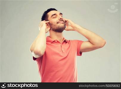 music, gesture and people concept - happy smiling man listening to music with imaginary headphones over gray background. happy man listening to music over gray background