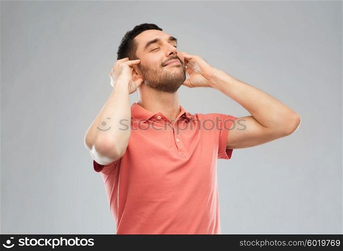 music, gesture and people concept - happy smiling man listening to music with imaginary headphones over gray background