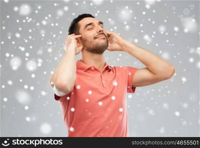 music, gesture, winter, christmas and people concept - happy smiling man listening to music with imaginary headphones over snow on gray background