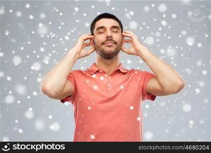 music, gesture, winter, christmas and people concept - happy smiling man listening to music with imaginary headphones over snow on gray background
