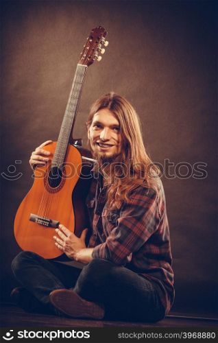 Music, hobby concept. Smiled guitarist with his instrument. Young man is sitting on the floor with nice shirt and guitar.