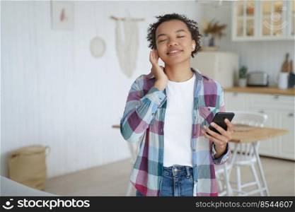 Music listening in airpods on mobile phone. Teenage girl enjoying music in wireless earphones. Afro young woman relaxing at home. Having fun and recreation alone. Music service website or app concept.. Teenage girl enjoying music in wireless earphones. Having fun and recreation concept.