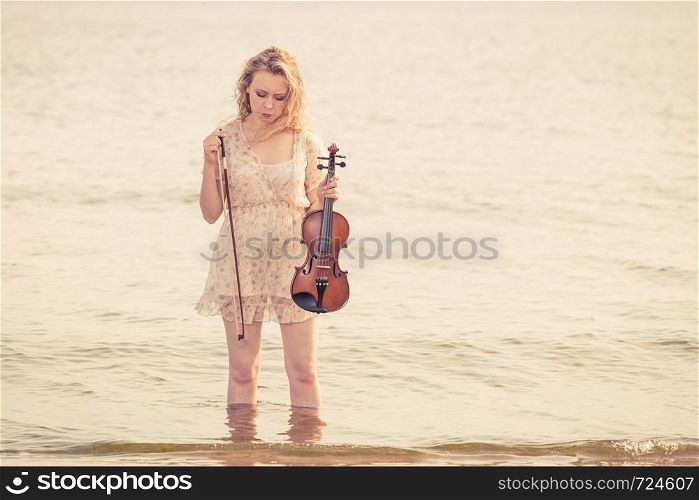 Music love, hobby and everyday passion concept. Woman on beach near sea holding violin playing in water. Woman on beach near sea holding violin