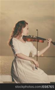 Music love, hobby and everyday passion concept. Woman on beach near sea playing on violin. Woman playing violin on violin near beach
