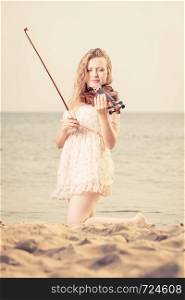 Music love, hobby and everyday passion concept. Woman on beach near sea playing on violin. Woman on beach near sea holding violin