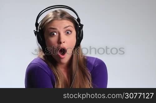 Music lover. Beautiful young woman in headphones listening music on white background. Happy brunette girl fooling around, making funny face and flirting with camera while enjoying her favorite song in earphones on the radio.