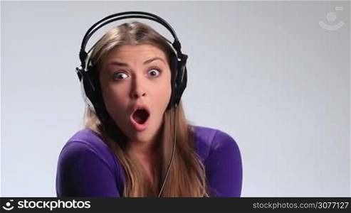 Music lover. Beautiful young woman in headphones listening music on white background. Happy brunette girl fooling around, making funny face and flirting with camera while enjoying her favorite song in earphones on the radio.