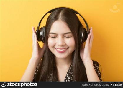 Music lover woman is enjoying with headset on yellow background