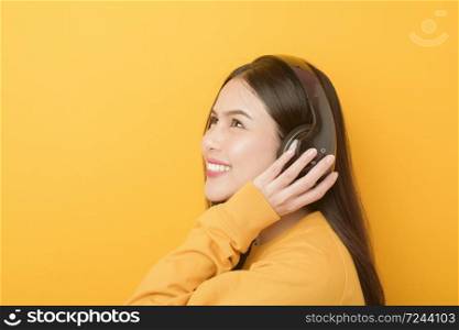 Music lover woman is enjoying with headset on yellow background