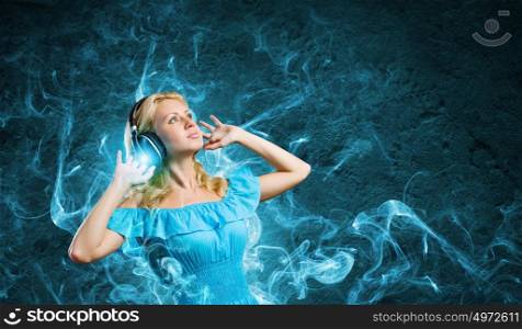 Music lover. Young lady in blue dress with headphones enjoying the music