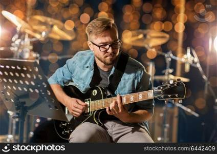 music, musical instruments and entertainment concept - male guitarist playing electric guitar at studio rehearsal over holidays lights background. man playing guitar at studio rehearsal