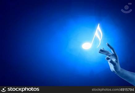 Music note. Close up of person hand touching music symbol on blue background