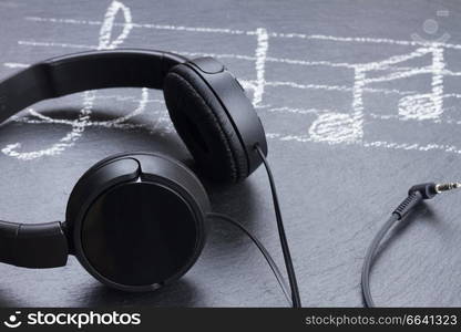 Music notes with treble clef and big headphones on black background. Music notes with  headphones 