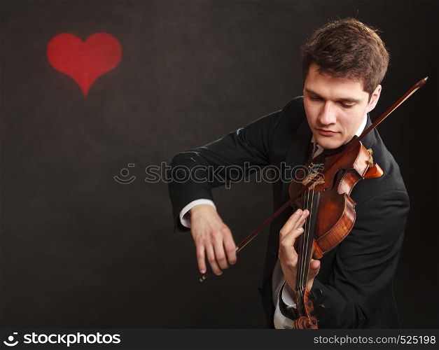Music passion, hobby concept. Romantic young man man dressed elegantly playing on wooden violin. Studio shot on dark background with red heart. Man man dressed elegantly playing violin