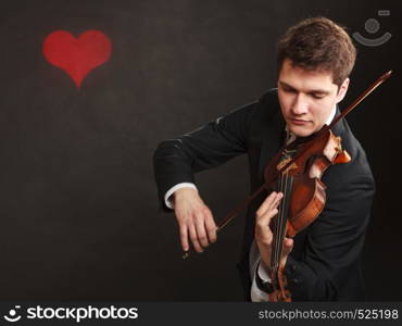 Music passion, hobby concept. Romantic young man man dressed elegantly playing on wooden violin. Studio shot on dark background with red heart. Man man dressed elegantly playing violin