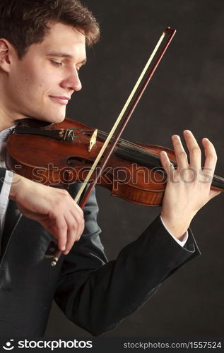 Music passion, hobby concept. Young man man dressed elegantly playing on wooden violin. Studio shot on dark background. Man man dressed elegantly playing violin