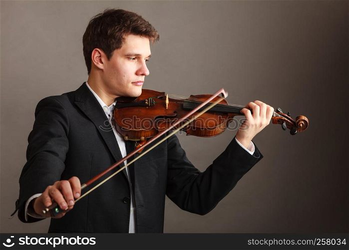 Music passion, hobby concept. Young man man dressed elegantly playing on wooden violin. Studio shot on dark background. Man man dressed elegantly playing violin