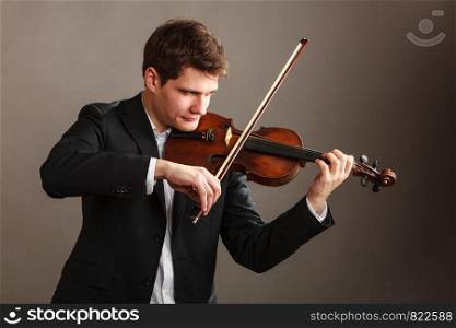 Music passion, hobby concept. Young man man dressed elegantly playing on wooden violin. Studio shot on dark background. Man man dressed elegantly playing violin