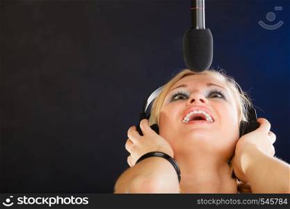 Music, passion, stage-fright concept. Blonde young woman singing to microphone and wearing big headphones on her head performing songs in studio.. Woman singing to microphone wearing headphones in studio