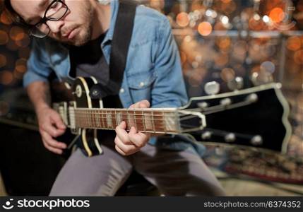 music, people and entertainment concept - male guitarist playing electric guitar at studio rehearsal over holidays lights background. musician playing guitar at studio or music concert